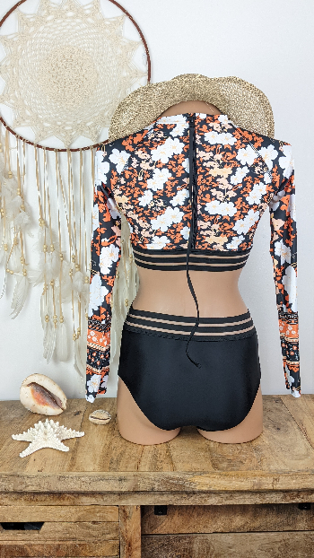 maillot de bain manche longue femme vue de dos fermeture éclair ouvert sur les hanches scindé sur le devant du bikini plage coloris bas noir haut fleuri orange blanc et noir