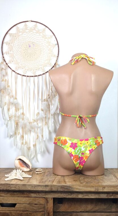 cette prise de vue montre un maillot de bain femme deux pièces à la coupe bikini brésilien femme son coloris est fleuri jaune vert et rose sur un fond blanc